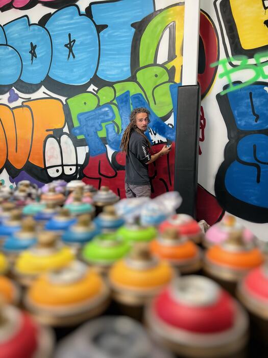 A graffiti artist at work behind a tray of spray cans