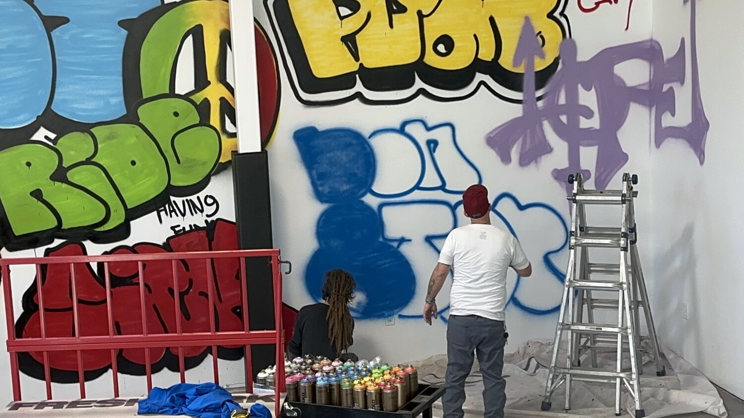 Two graffiti artists painting the Life Shop wall during build-out