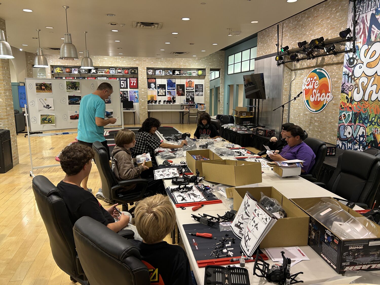Teens building RC kits together at the class tables at Life Shop, with the logo and graffiti mural behind them