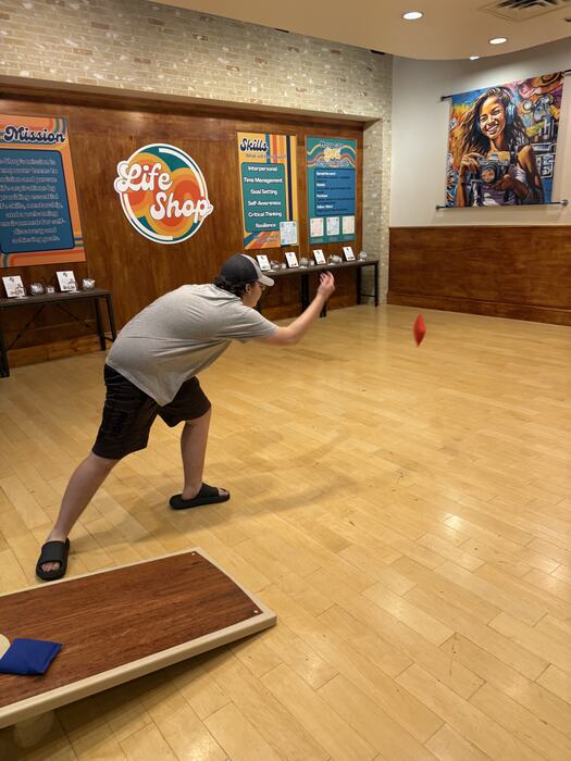 A teen mid-throw during a cornhole game at Life Shop