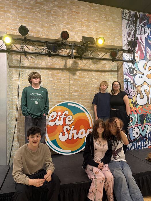 A group of teens by the Life Shop logo wall