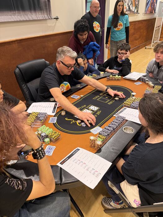 A staff member running the poker table for a group of teens
