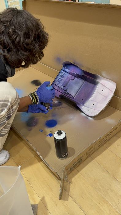 A teen spray-painting an RC car body in the paint booth