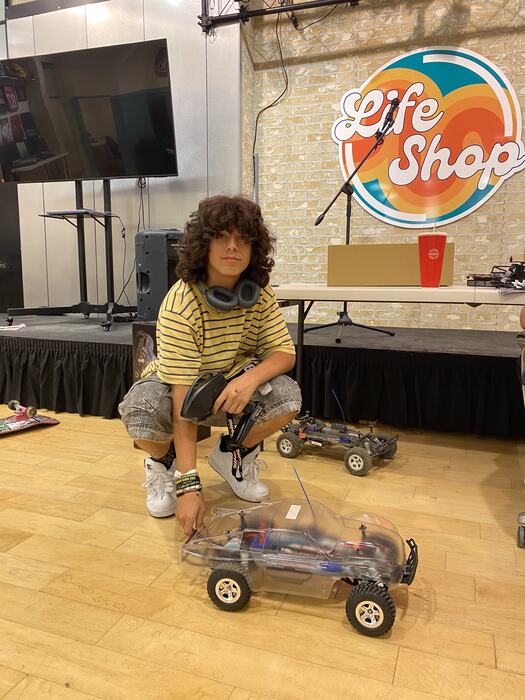 A teen with an RC buggy in front of the Life Shop logo